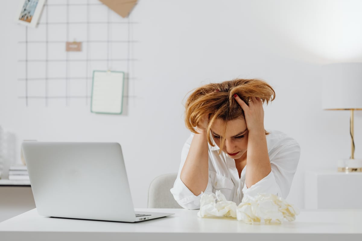 Frustrated woman at desk with laptop, head in hands